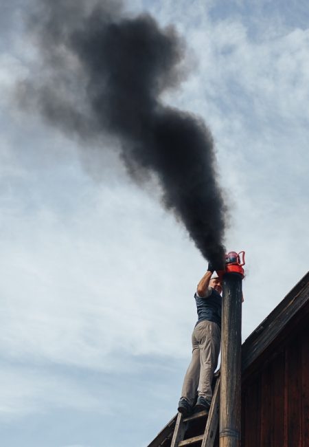 Chimney sweep cleaning a chimney standing balanced on the apex of a house roof lowering equipment down the flue